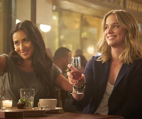 Two women sitting at a table in a restaurant, smiling and raising wine glasses.