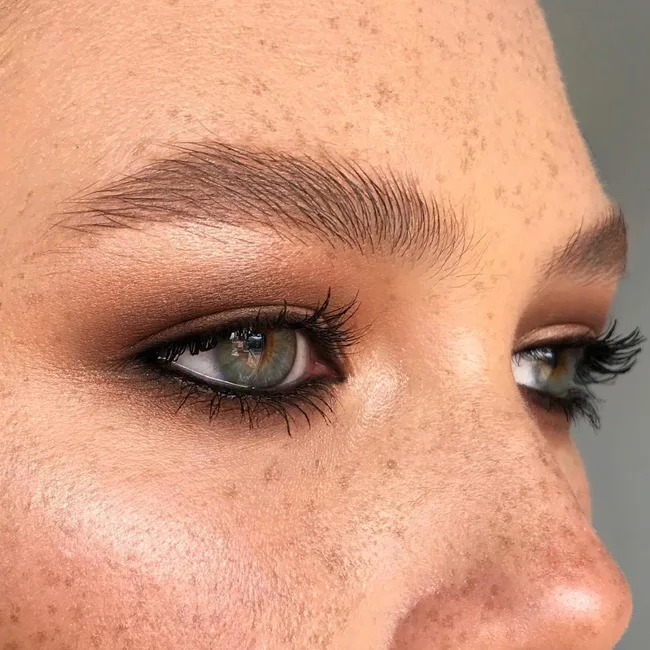 Close-up of a person's eye with green iris, freckles, and shimmery brown eyeshadow.