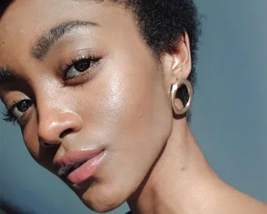 Close-up of a person with natural short hair, wearing hoop earrings, against a neutral background.