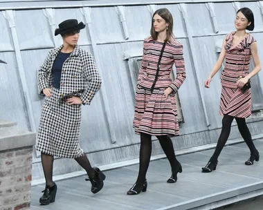 Models walking on a rooftop catwalk wearing stylish patterned outfits and black tights.