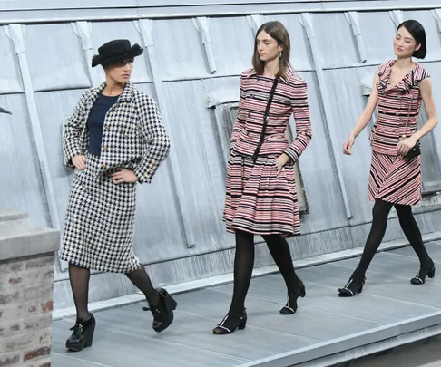 Models walking on a rooftop catwalk wearing stylish patterned outfits and black tights.