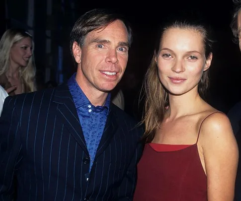 A man in a pinstripe suit and a woman in a red dress smiling at a public event with dim lighting.