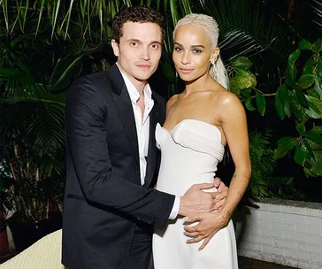 A couple poses together at their wedding, surrounded by lush greenery.