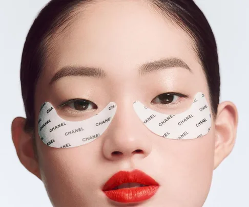 Woman with red lipstick wearing Chanel under-eye patches on a white background.