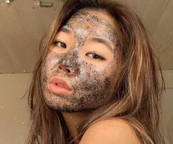 Young woman with long hair, covered in glitter and stars on her face, posing indoors against a wooden ceiling.