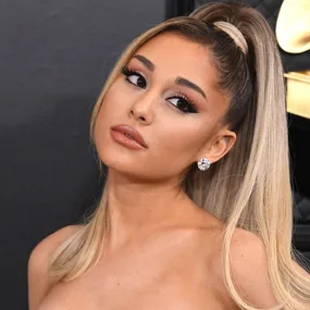 Ariana Grande at the Grammys in an elegant dress, hair in a high ponytail, with striking makeup and diamond earrings.