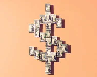 Dollar bills arranged in a dollar sign shape on a peach background.