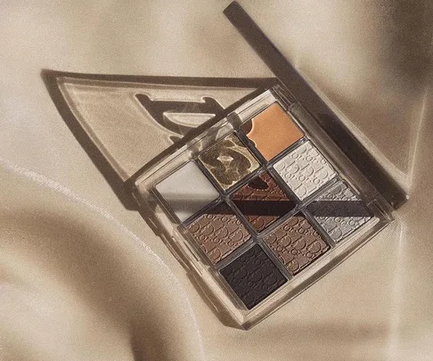 A Dior eyeshadow palette featuring cool-toned shades in a grid layout on a beige satin background.