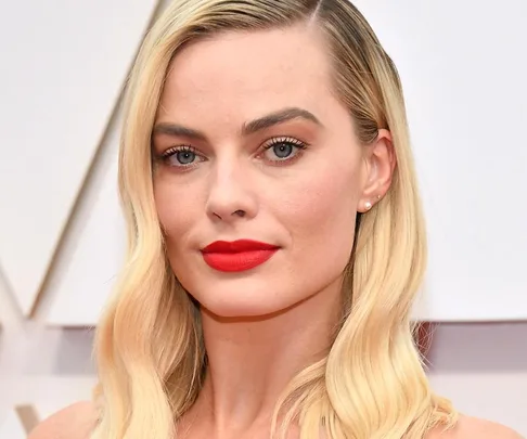 Blonde woman with red lipstick and pearl earrings at Oscars 2020, wearing a sleek hairstyle and neutral makeup.