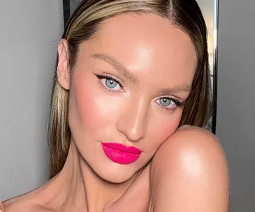 A woman with light hair wearing bright pink lipstick against a neutral background.