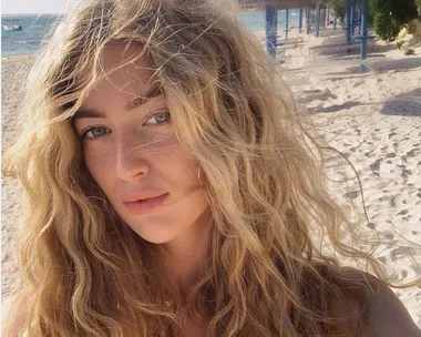 Woman with long wavy blonde hair on a sunny beach.