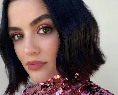 A person with a short bob hairstyle and pink sequined top gazes at the camera, showcasing long, curled eyelashes.