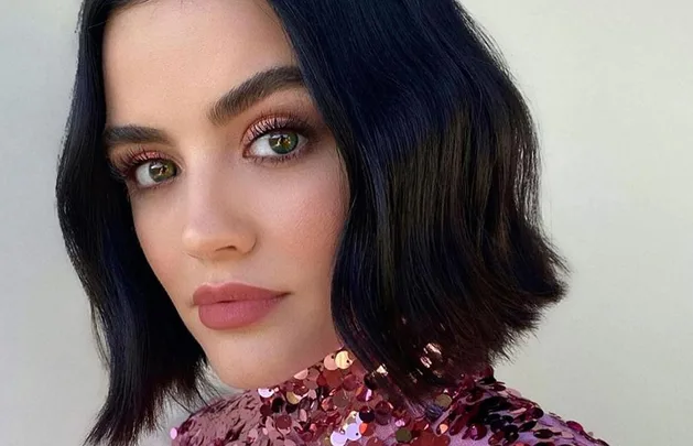 A person with a short bob hairstyle and pink sequined top gazes at the camera, showcasing long, curled eyelashes.