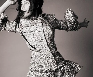 Phoebe Tonkin in a textured dress and stylish hat, energetically posing against a plain backdrop.