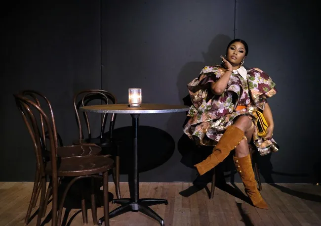 Woman in a floral dress and knee-high boots sitting in a dimly lit room next to a table with a candle.