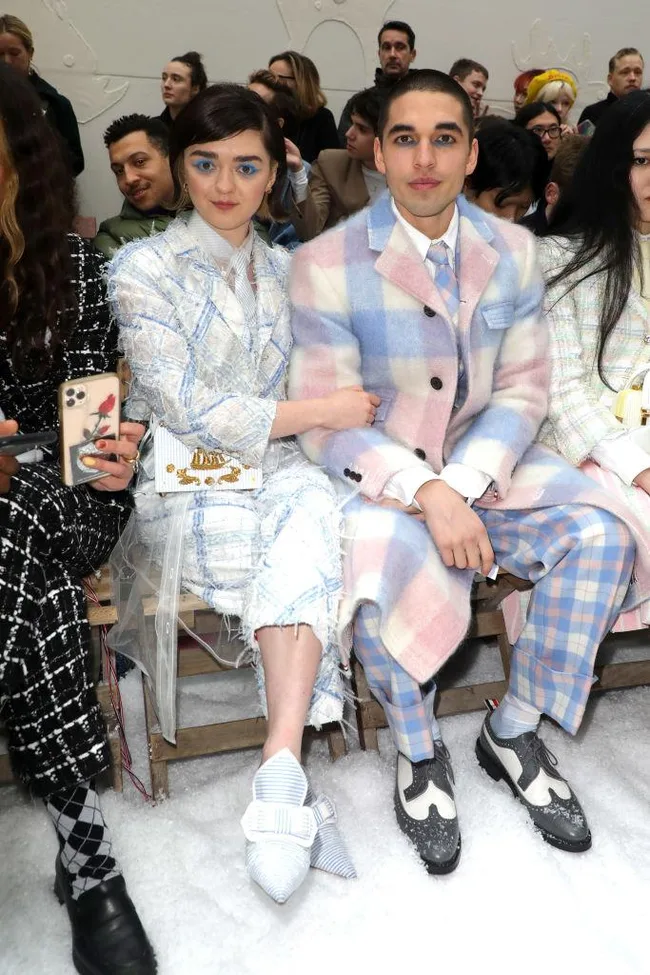 Fashionably dressed individuals seated at a runway show, amidst a crowd of attendees, showcasing stylish outfits.