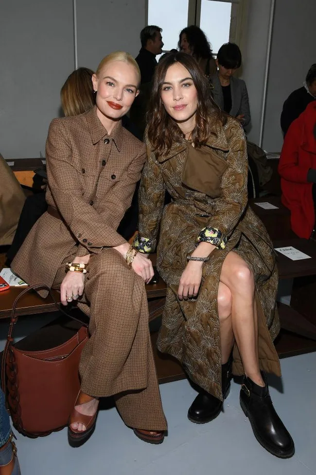 Two women sitting in fashionable brown outfits at a fashion event.