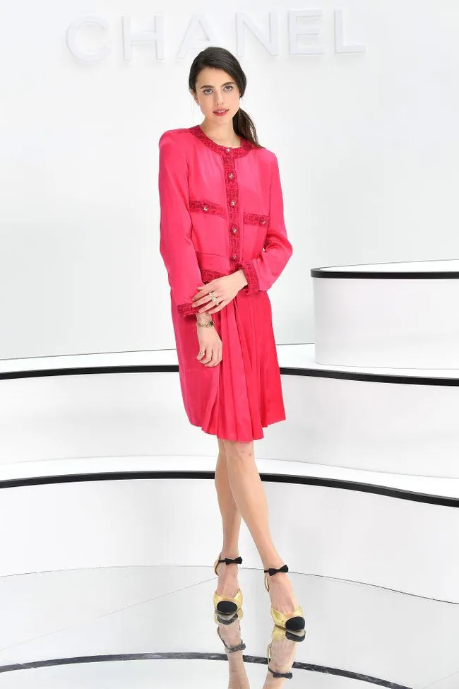 Woman in pink Chanel outfit with black and yellow heels standing in front of a Chanel sign.