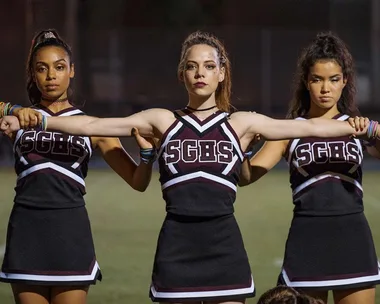 Cheerleaders in black uniforms with "SGBS" logo stand side by side on a field at night.