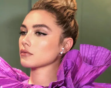 Person with an elegant updo hairstyle, wearing a dramatic purple ruffled dress and diamond earrings.