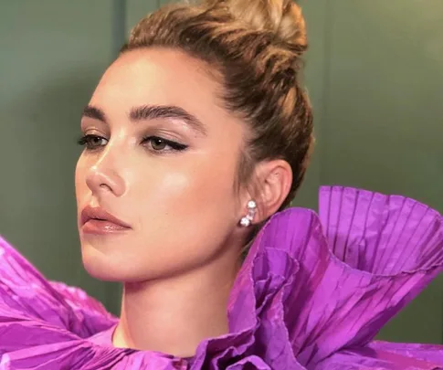 Person with an elegant updo hairstyle, wearing a dramatic purple ruffled dress and diamond earrings.