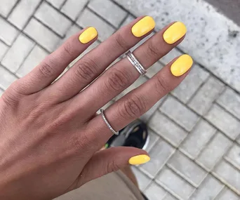 Hand with yellow gel nail polish and silver rings on a tiled background.