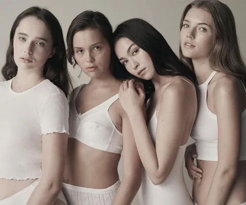 Four women in white tops pose closely together against a neutral background.