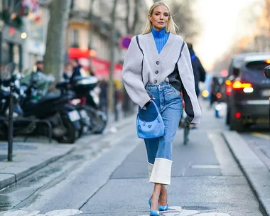 Woman in street style wearing a gray jacket, blue turtleneck, cropped flare jeans, and blue heels with a matching bag.