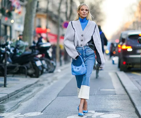 Woman in street style wearing a gray jacket, blue turtleneck, cropped flare jeans, and blue heels with a matching bag.