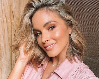 Smiling woman with shoulder-length blonde hair in a pink shirt, posed in front of a wooden background.