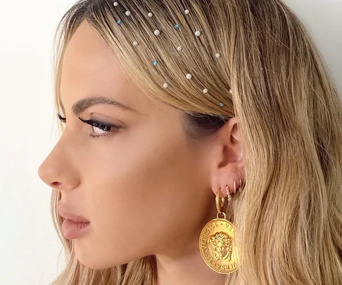 Blonde woman with pearl and bead hairpins and large gold coin earring, profile view.