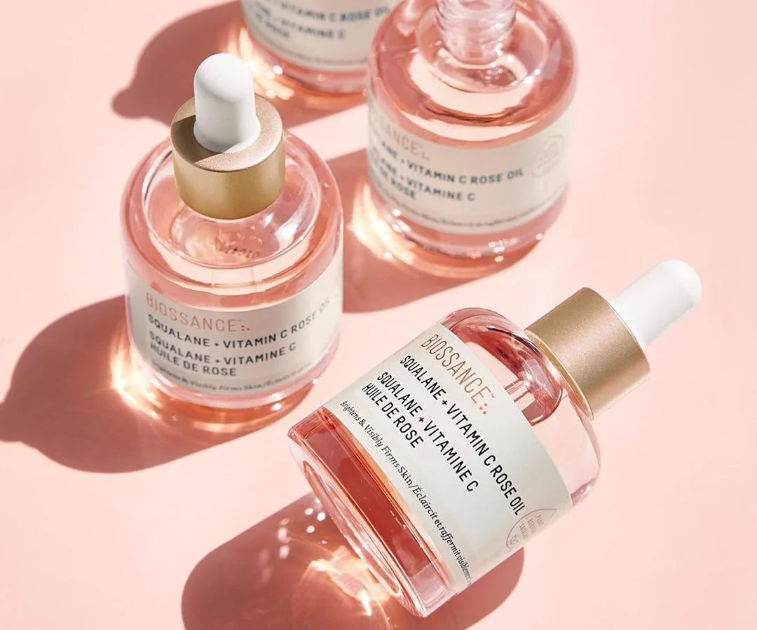 Bottles of Biossance Squalane + Vitamin C Rose Oil on a pink background.