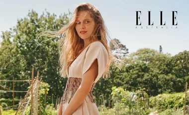 Teresa Palmer in a beige dress stands in a garden setting, windy hair, smiling at the camera, Elle Australia logo visible.