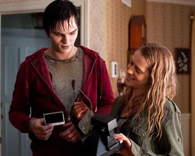 A young man and woman smile as they look at a Polaroid photo. The man is wearing a red hoodie and the woman holds the camera.