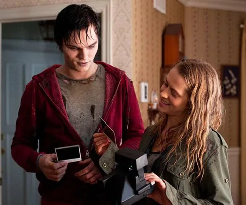 A young man and woman smile as they look at a Polaroid photo. The man is wearing a red hoodie and the woman holds the camera.