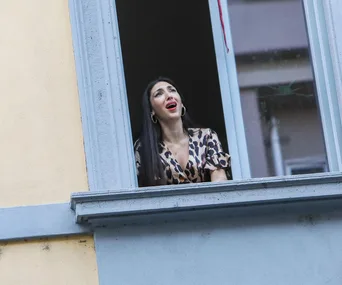 Woman singing from an open window in a building, wearing a leopard-print dress.