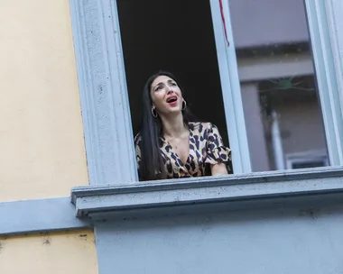 Woman singing from an open window in a building, wearing a leopard-print dress.