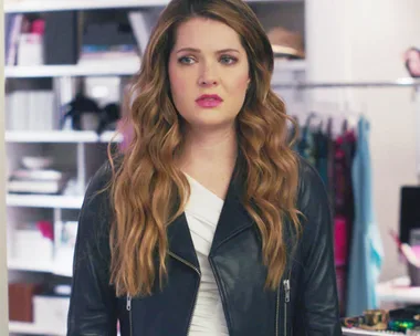 A woman with long hair in an office setting, looking concerned while dressed in a black leather jacket.