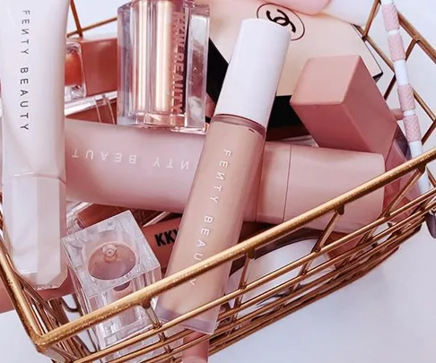 Basket containing Fenty Beauty makeup products, including lipsticks and foundation, in a neat arrangement.