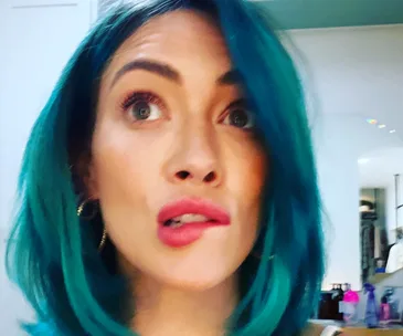 Person with vibrant blue hair looking upward with a surprised expression.