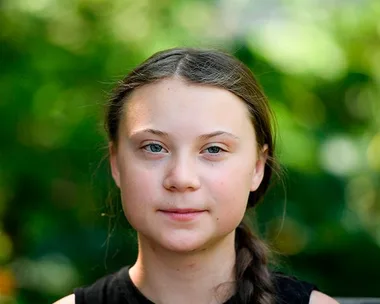 Young girl with braided hair standing outdoors against a blurred green background.