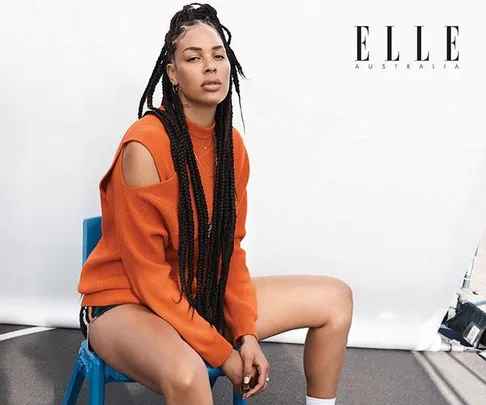 Liz Cambage sitting on a blue chair wearing an orange sweater with long braids, ELLE Australia branding in corner.