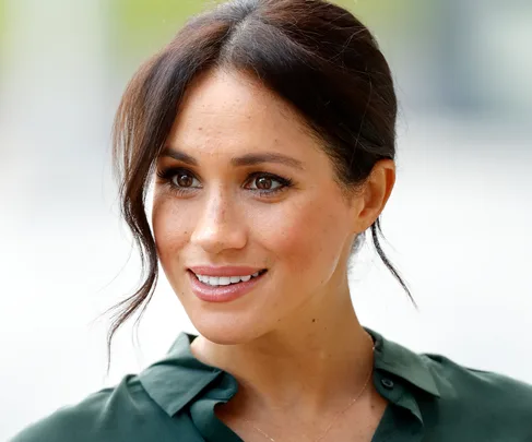 Woman with brown hair styled in a messy bun, smiling, wearing a green blouse.