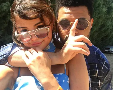 A man and woman wearing sunglasses, outdoors, embrace closely with a playful demeanor.