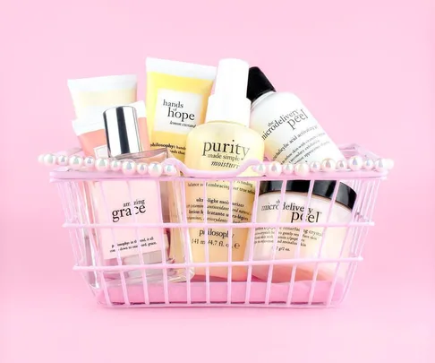 A pink basket with assorted skincare products labeled "philosophy" against a pink background.