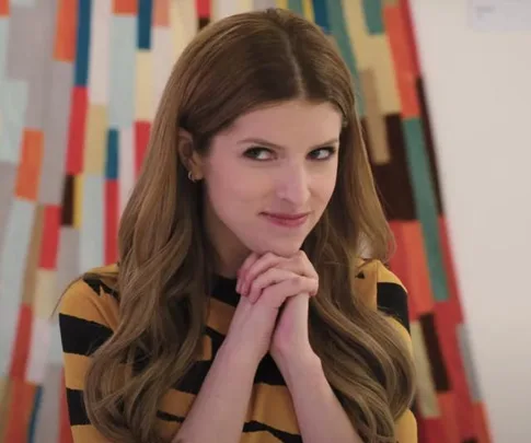A woman with long hair and a thoughtful expression, hands clasped near her face, in front of a colorful abstract background.