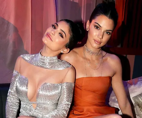 Two women in stylish outfits sitting together, one in silver, one in orange, posing for a photo.