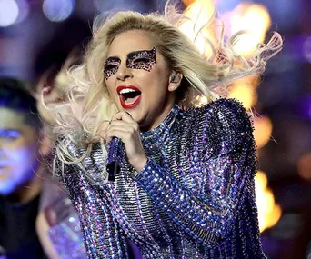 Singer in sparkling outfit with dramatic eye makeup performing energetically on stage.