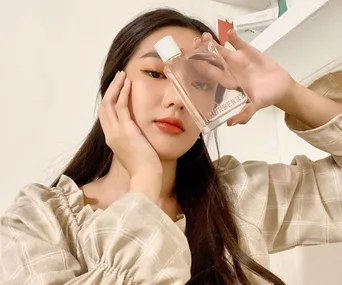 Person holding a Burberry perfume bottle close to their face, wearing a checked shirt.