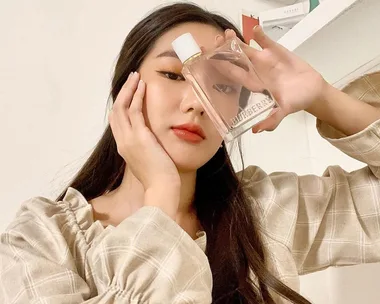 Person holding a Burberry perfume bottle close to their face, wearing a checked shirt.